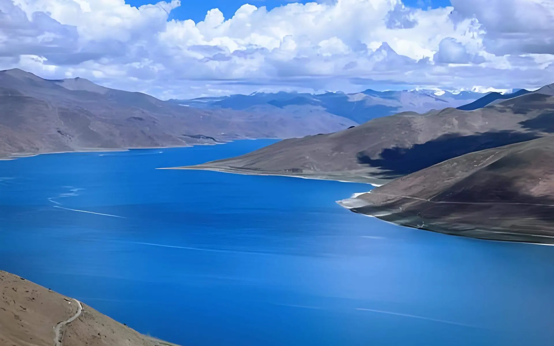 The turquoise water of Yamdrok Lake winding between hills under snow peaks